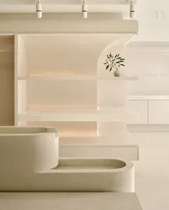 A modern minimalist library with minimalist white shelves made of plaster, light-colored wooden floors and a white curtain.