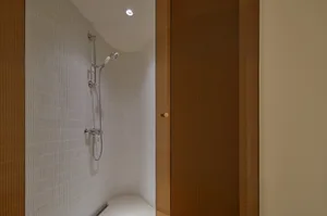 Minimalist bathroom with white tiled walls and floor, featuring a walk-in shower.