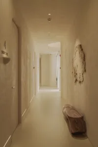 Modern minimalist corridor with concrete walls and floor, featuring a wooden bench and a textured wall hanging.