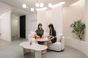 Two women sitting on a white sofa in a minimalist office setting.