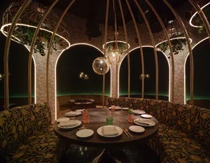 A round dining table surrounded by booth seating in a modern restaurant interior with metal arches and textile upholstery.