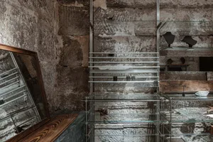 An industrial-style glass display case against a textured stone wall, featuring glass shelves and metal supports.
