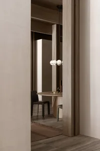 A modern minimalist dining room with a round wooden table and black chairs under a chandelier.