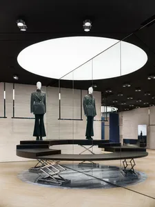 A modern fashion display featuring two mannequins dressed in designer clothing and a black ceiling with a circular light fixt