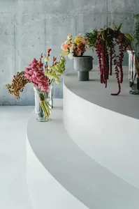 現代室內空間，彩色花卉插花置於玻璃花瓶中，擺放在高起的弧形水泥平台上。