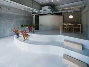 A modern living room with a concrete floor and curved stage, featuring flowers on a white platform.