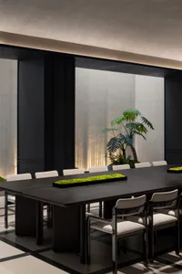 A modern conference room featuring a long black table surrounded by white chairs, with a central green plant arrangement and 