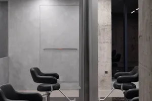 現代極簡美髮沙龍室內，擁有光滑的混凝土牆面與黑色座椅。