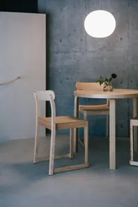 A minimalist interior with wooden chairs and a round table, featuring a round light fixture hanging overhead.