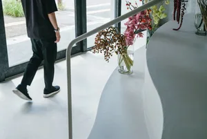 Person walking along a minimalist, white, curved wall with floral arrangements in glass vases.