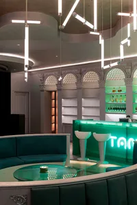 A modern retail bar with glass counters, metal elements, and plastic stools, featuring a green aesthetic and illuminated sign