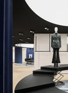 A modern retail space featuring a fashion exhibit with a mannequin wearing a stylish jacket and pants on a curved black platf