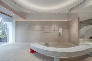 A minimalistic retail space featuring white walls, concrete flooring, and a sleek, curved seating area in a contemporary desi