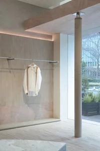 A modern clothing store display featuring light-colored concrete walls and a single white shirt hanging on a rod.
