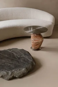 A modern, curved marble side table with a round, metallic top and a vase-like base.