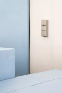 A minimalist doorbell mounted on a white wall, featuring metallic material.