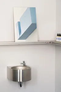 A modern industrial bathroom featuring a metal sink and shelf with a framed blue artwork on the wall.