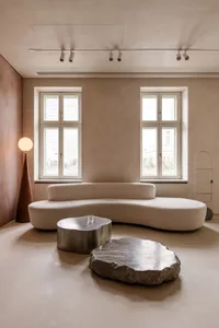 Modern living room featuring a curved white fabric sofa, metallic coffee table, and stone slab.