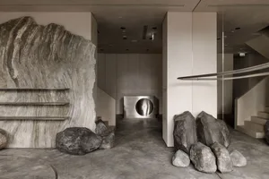 A modern lobby with concrete walls and large rocks, featuring a metal column with a circular opening.
