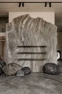 A modern interior design featuring a large, textured marble wall with minimalist shelves and decorative rocks.