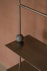 Modern metallic shelving system with geometric design and stone sphere on top.