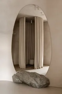 A minimalist interior with soft, neutral-colored fabric curtains and a large rock-like sculpture.