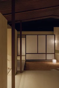 A minimalist interior featuring paper screens on wooden walls, with a small illuminated cube on the floor.