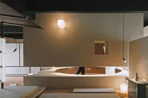 A minimalist interior space featuring concrete walls and floors, with a person walking in the background.