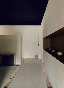 A minimalist living room with concrete walls and floor, featuring a modern shelf with bowls and a blue-and-white vase.