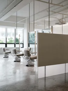 An industrial-style salon with concrete floor, metal chairs, and glass partitions.