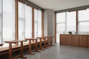 A minimalist restaurant interior with wooden tables and large glass walls allowing natural light to fill the space.