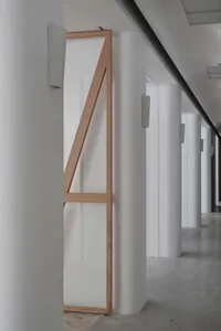 A minimalist corridor with concrete walls, white columns, and a wooden frame