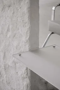 Modern minimalist floating shelf made of clear glass with metal hardware against a textured concrete wall
