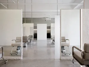 A minimalist hair salon featuring concrete flooring and white walls, with mirrors on the back wall.