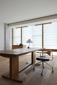 A modern minimalist home office space featuring a wooden desk, chair, and lamp.