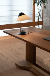 A modern minimalist desk made of wood with a white table lamp on it.