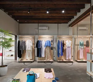 Modern clothing retail store with wooden walls and concrete floor, featuring clothes on shelves and racks.