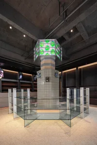 A modern art installation featuring glass, concrete, mosaic patterns, and illuminated elements.