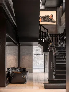 A modern office space featuring a mix of concrete and wooden materials, with a black leather sofa and a staircase.