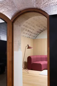 A room with an arched doorway featuring a textured concrete wall, wooden flooring, and a modern sofa in a geometric, minimali