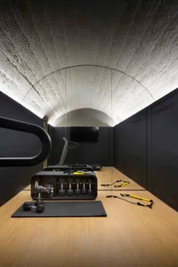 A modern gymnasium with industrial design elements, concrete walls, and minimalist aesthetic. Features include weights, exerc