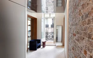 Modern interior designed with concrete and brick walls, featuring a sleek, black sofa and a glass door leading to a balcony.