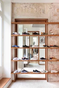 Modern shoe shop display featuring a variety of sneakers on wooden shelves against a rough-hewn stone wall with a terrazzo fl