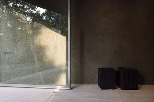 A modern industrial-style window made of glass, with a textured wall and black stool-like objects in the foreground.
