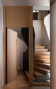 A modern interior space featuring a wooden staircase with concrete walls and sunlight.