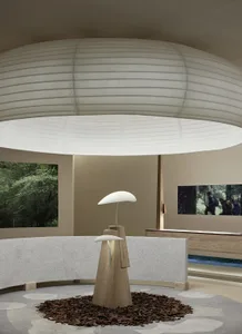 A minimalist lamp with a wooden base and a concrete counter is surrounded by a white fabric ceiling and a forest view.