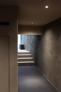 A modern, minimalist hallway with concrete stairs and walls, illuminated by recessed lighting.