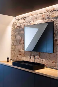 A modern bathroom featuring a black sink and faucet on a wooden counter against a brick wall with a skylight.
