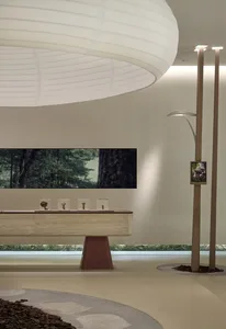 A modern exhibition space featuring a circular light fixture, a wooden table with glass cases, and digital screens displaying