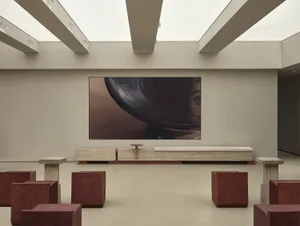 A minimalist concrete lobby with seating, a low bench, and a large screen displaying a bowl.